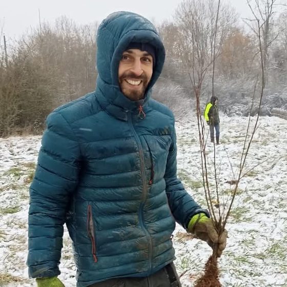 Samuel Claisse, souriant, un jeune arbre à racines nues à la main, lors d’une plantation sous la neige